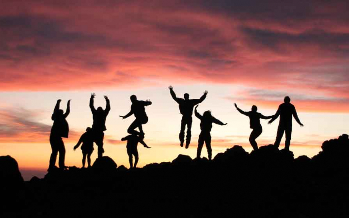 the silhouette of nine people jumping into the air at sunset